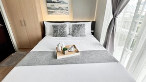 Una habitación de hotel con una cama, una mesita de noche de madera con una bandeja de desayuno, una ventana con cortinas y un cuadro en la pared.