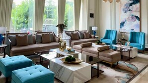Amplia sala de estar con un gran ventanal, un juego de sofás, una mesa de centro y un sillón azul.