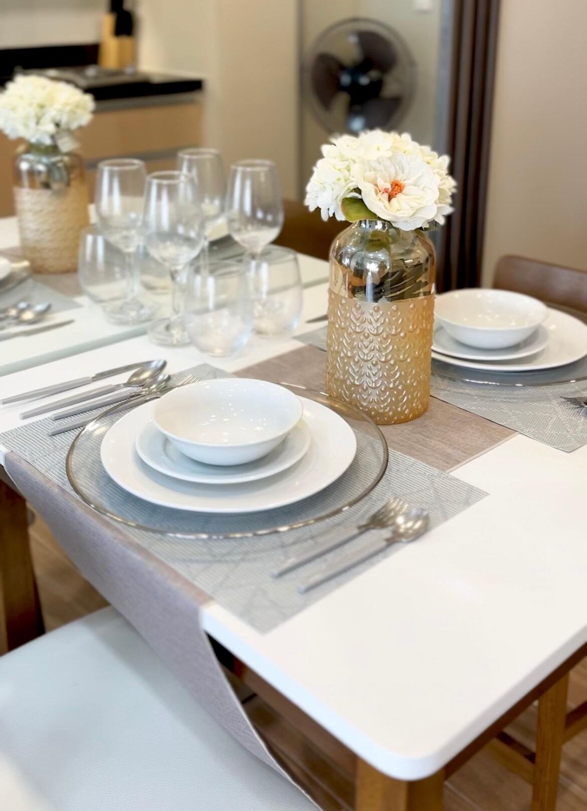 A dining table set with plates, glasses, and cutlery, with a vase of flowers on the table.