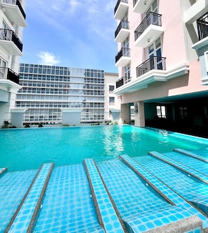 A swimming pool with blue tiles and steps leading into it, surrounded by multi-story buildings with balconies. - Room-elegant Studio in Saint Dominique (Iloilo)