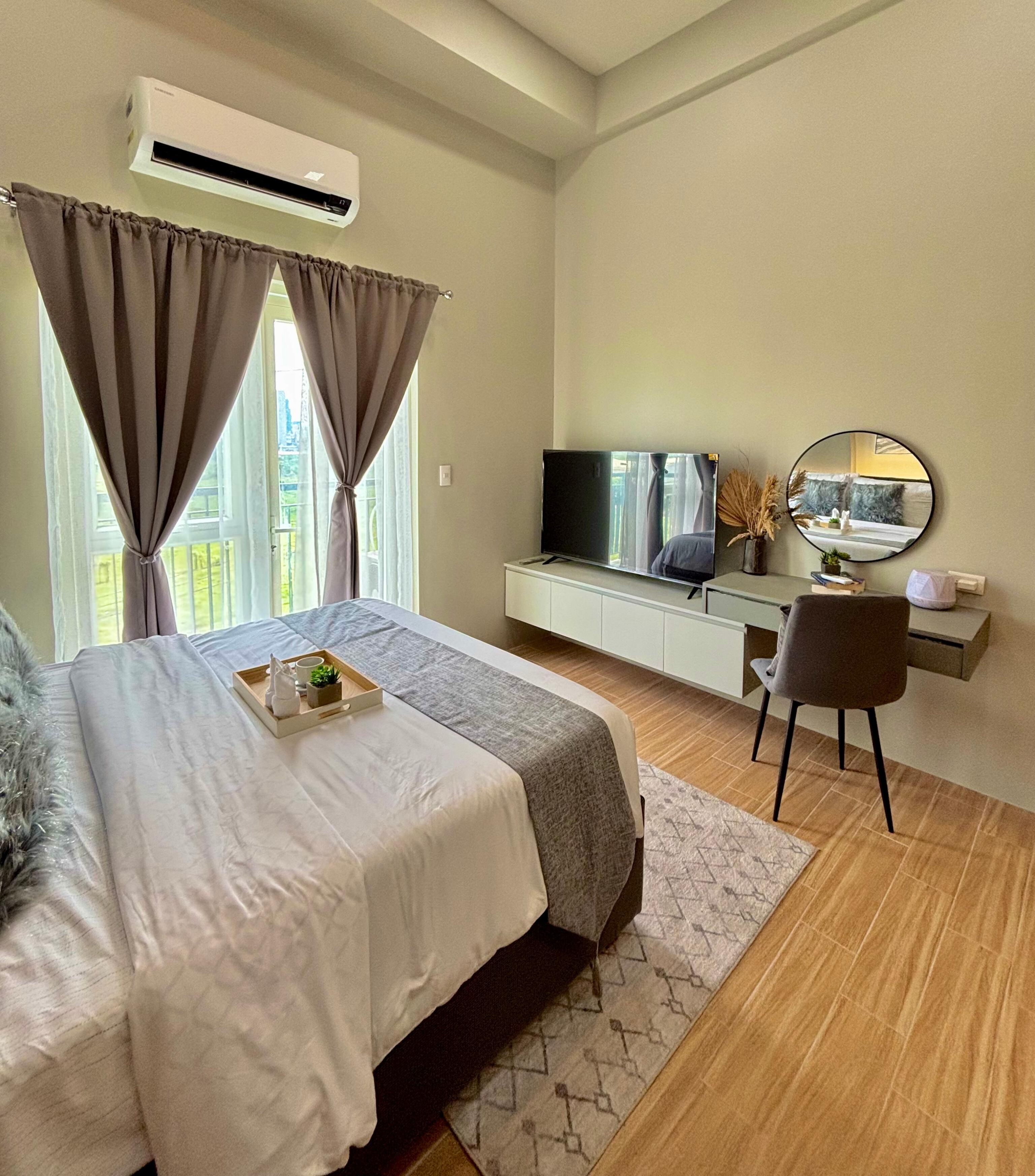 A modern bedroom with a bed, a desk, a TV, and a mirror.