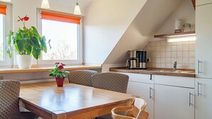 Una cocina moderna con una mesa y sillas de madera, una cafetera y un ventanal con cortinas naranjas.