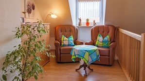 Una habitación acogedora con dos sillones de cuero, una mesita con mantel a cuadros, un armario de madera y una planta en maceta.