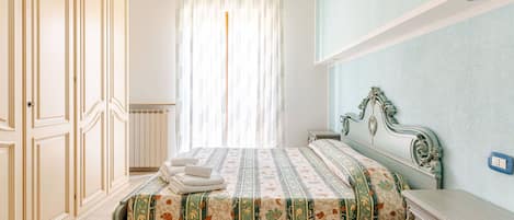 Ein Schlafzimmer mit einem Bett, einem Schminktisch, einem Heizkörper und einem Fenster mit Vorhängen.