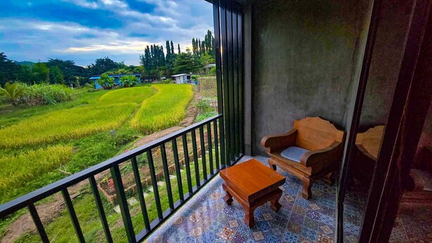 A balcony with a view of a green field, a wooden chair, and a small table. - Zuu Tee Organic Farm & Roastery (Pai)