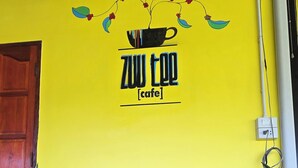A dining table with a basket of fried food and a cup of sauce, a wooden headboard, and a yellow wall with a cafe sign. - Zuu Tee Organic Farm & Roastery (Pai)