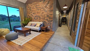 A modern living room with a brick wall, wooden flooring, a sofa, a coffee table, and a view of the outdoors. - Zuu Tee Organic Farm & Roastery (Pai)