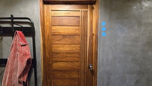 A wooden door with a metal handle, a towel hanging on a rack, and a wall with three blue stickers. - Zuu Tee Organic Farm & Roastery (Pai)