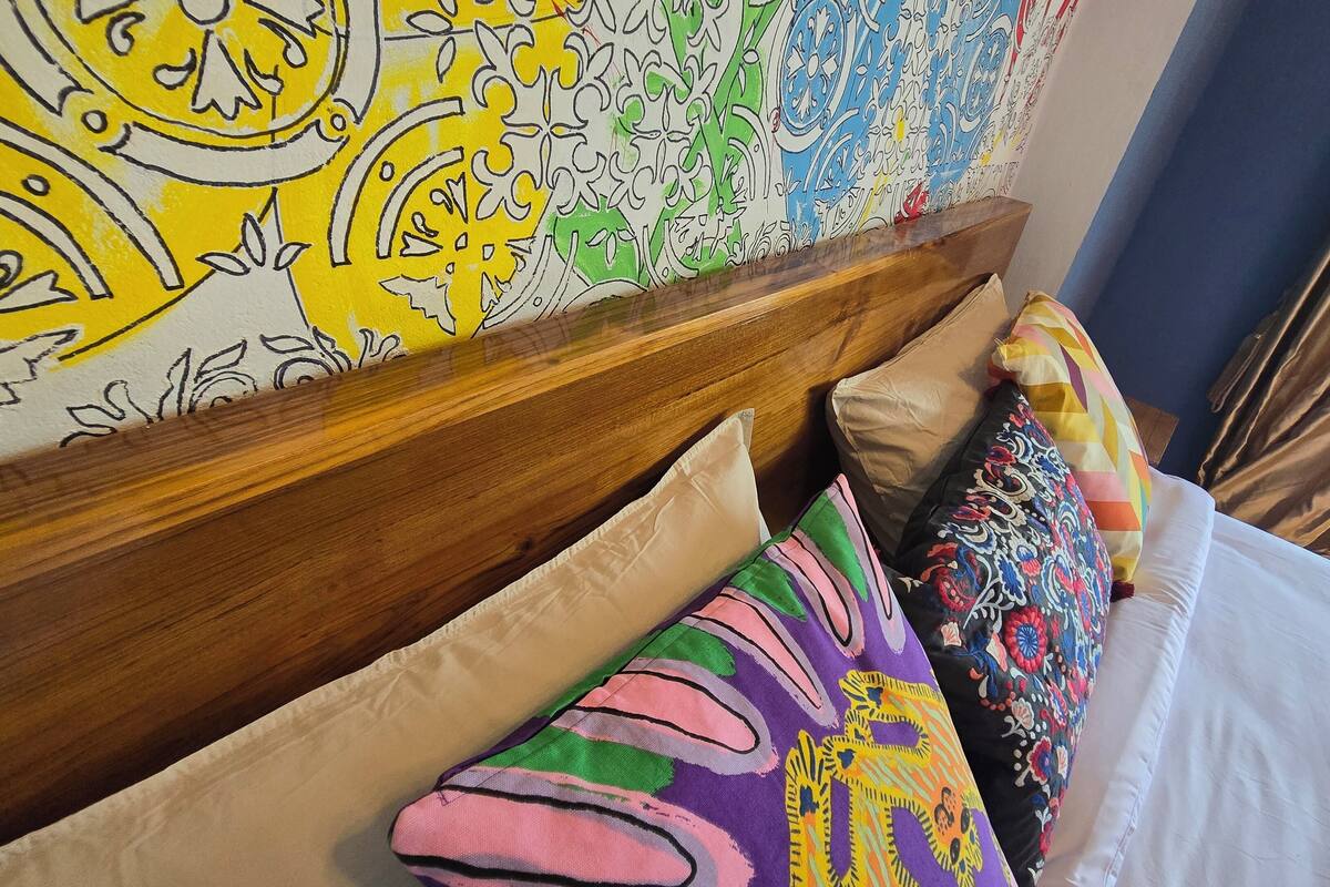 A hotel room with a wooden headboard, colorful pillows, and a vibrant abstract wall mural.