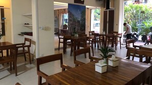 A spacious dining area with wooden tables and chairs, a large painting on the wall, and a view of the outdoors through a glass door. - Amara Palace (Phnom Penh)