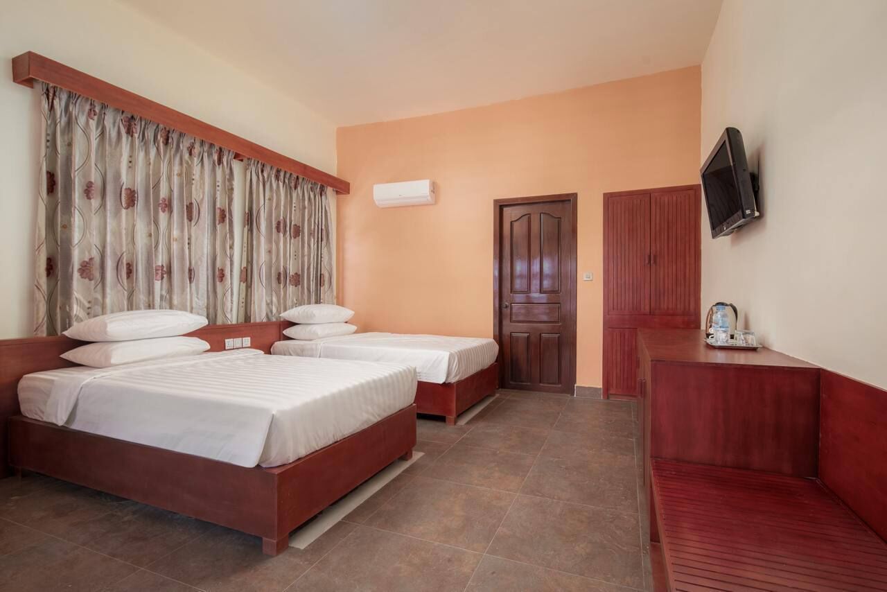 A hotel room with two beds, a TV, an air conditioner, and a wooden bench.