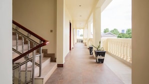 A long, narrow corridor with a wooden staircase on the left and potted plants on the right. - Amara Palace (Phnom Penh)