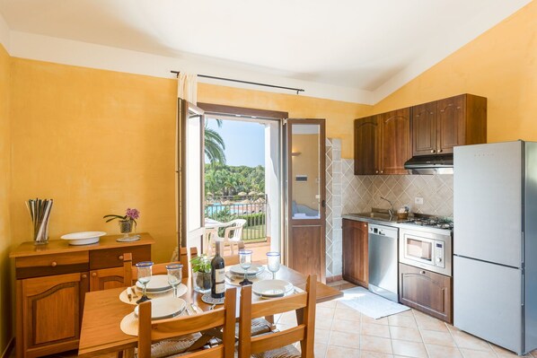 A kitchen with wooden cabinets, a stainless steel refrigerator, and a dining area with a table set for four.
