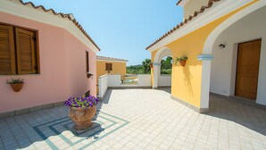 A courtyard with tiled flooring, a large potted plant, and buildings with arched doorways and wooden shutters. - Residence in Orosei with 2 bedrooms sleeps 6 (Orosei)
