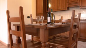 Una mesa de madera con cuatro sillas, una botella de vino y tres copas sobre un mantel individual.