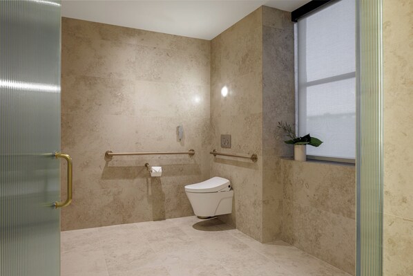 A bathroom with a toilet, grab bars, a window, and a plant. - The Moore Miami  (Miami)