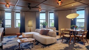 A modern living room with a sectional sofa, a round dining table with chairs, and large windows with curtains.