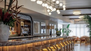 A modern bar area with a long counter, wooden stools, and a ceiling light fixture.
