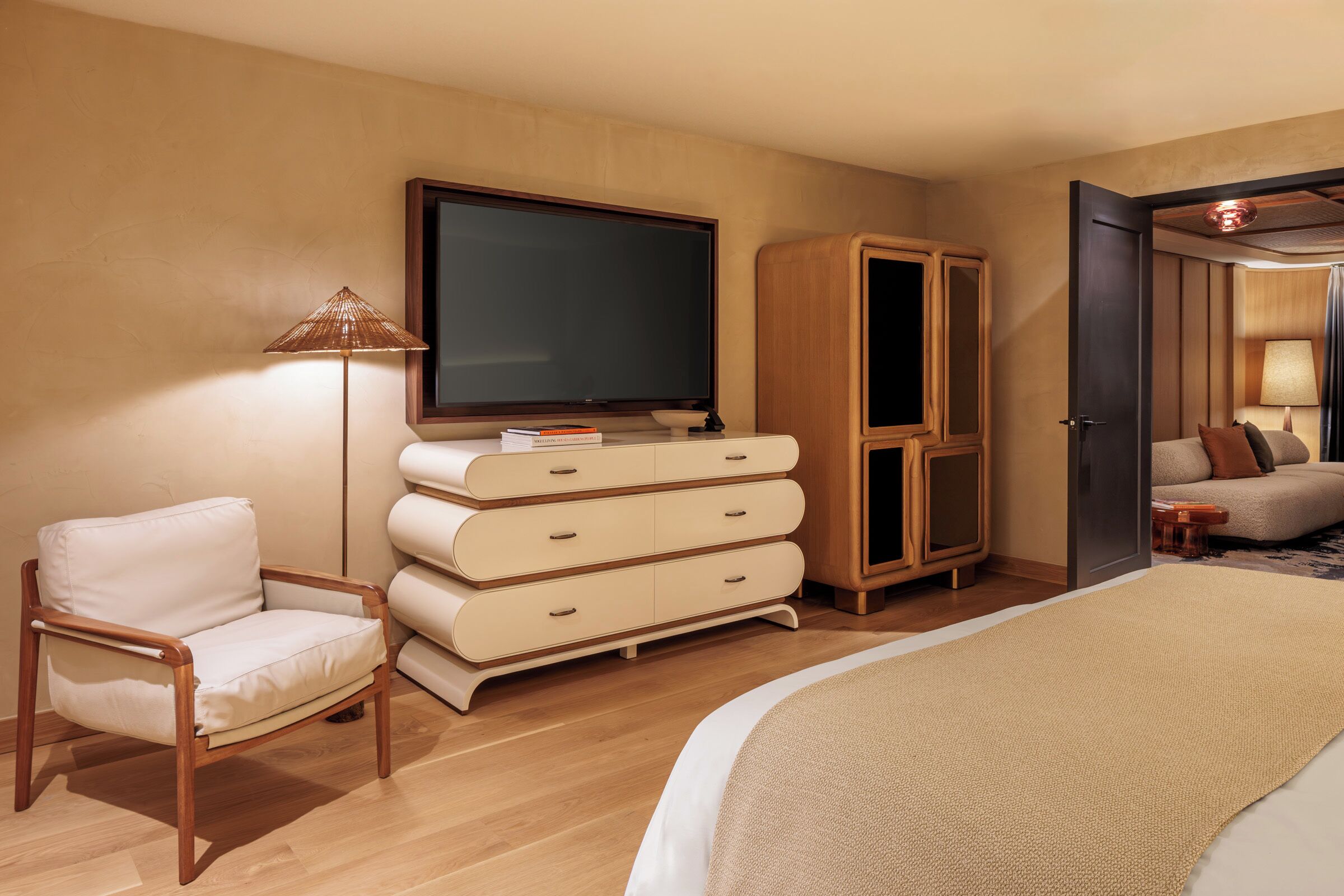 A hotel room with a bed, a TV, a wooden wardrobe, a chair, and a lamp.