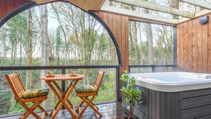 Una terraza de madera con un jacuzzi, dos sillas y una mesa con tazas.