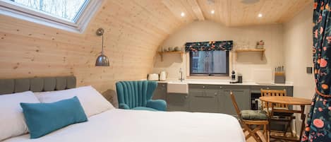 A cozy cabin interior with a bed, a dining table, a kitchen area, and a window with a view.