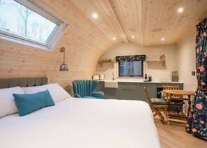 L’intérieur chaleureux d’un chalet comprend un lit, une table à manger, un coin cuisine et une fenêtre donnant sur un paysage agréable.