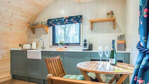 Interior acogedor de una cabaña con techo de madera, una cocina con ventana, una mesa de comedor con sillas y una botella de vino.
