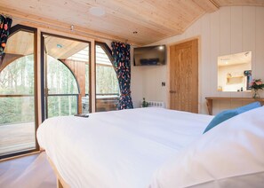 A bedroom with a bed, a TV, a mirror, and a view of the outdoors.