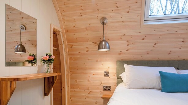 Habitación con paneles de madera, una cama, mesita de noche, espejo e iluminación colgante.