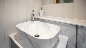 Un baño con lavamanos de mármol blanco, dispensador de toallas y soporte para papel higiénico sobre una encimera blanca.