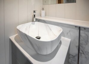 A bathroom with a white marble sink, a towel dispenser, and a toilet paper holder on a white countertop.