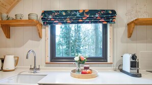 Una cocina con ventana, un lavamanos, un hervidor, una cafetera y un frutero.