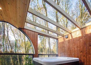 Una cabaña de madera con jacuzzi, ventanas grandes y vistas al bosque.