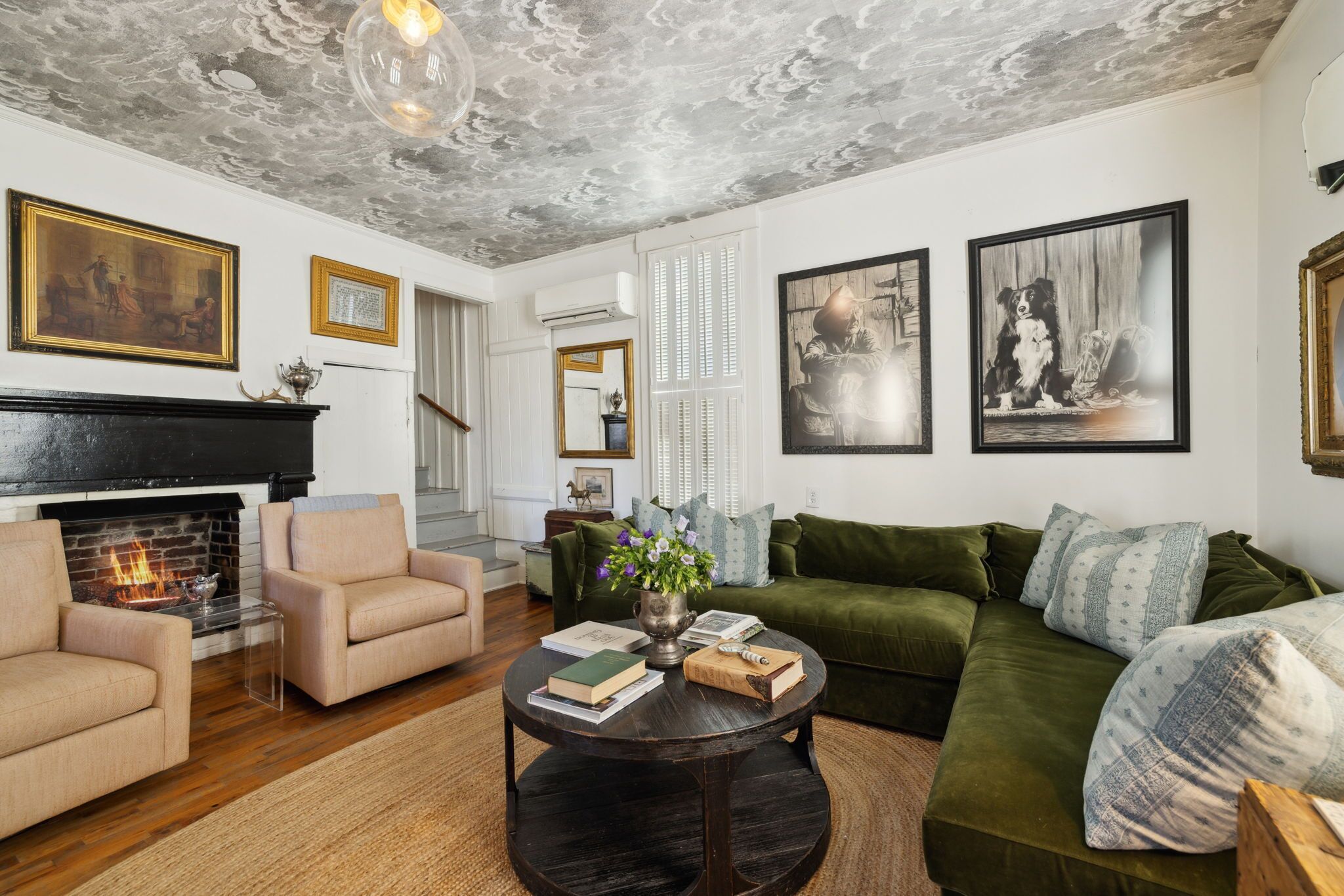Ein Wohnzimmer mit Kamin, grünem Sofa und Kunstwerken an den Wänden.
