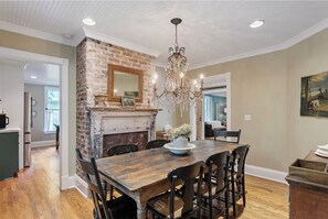 Cozy dining area with a wooden table and chairs, a chandelier, and a brick fireplace.