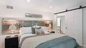 Un dormitorio con cama, mesitas de noche, cómoda, perchero y puerta corrediza.