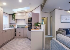 Une cuisine moderne dotée d’appareils électroménagers intégrés, d’un parquet en point de Hongrie et d’un petit îlot central agrémenté d’une plante.
