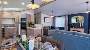 Eine moderne Küche mit integrierten Geräten, ein Essbereich mit Tisch für vier Personen und eine Wohnfläche mit Sofa und Kamin.