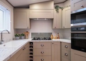 A modern kitchen with beige cabinetry, a built-in stove, and a black oven. - Deluxe modern and contemporary luxury lodge perfect for a relaxing escape. (Workington)