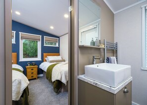 Une chambre avec deux lits, une salle de bain avec un lavabo blanc et un miroir qui reflète la pièce.