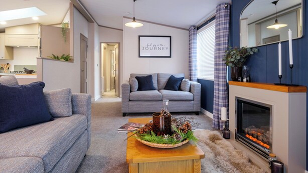 Ein modernes Wohnzimmer mit einer Couch, einem Couchtisch mit dekorativer Dekoration, einem Kamin und einer Küche im Hintergrund.