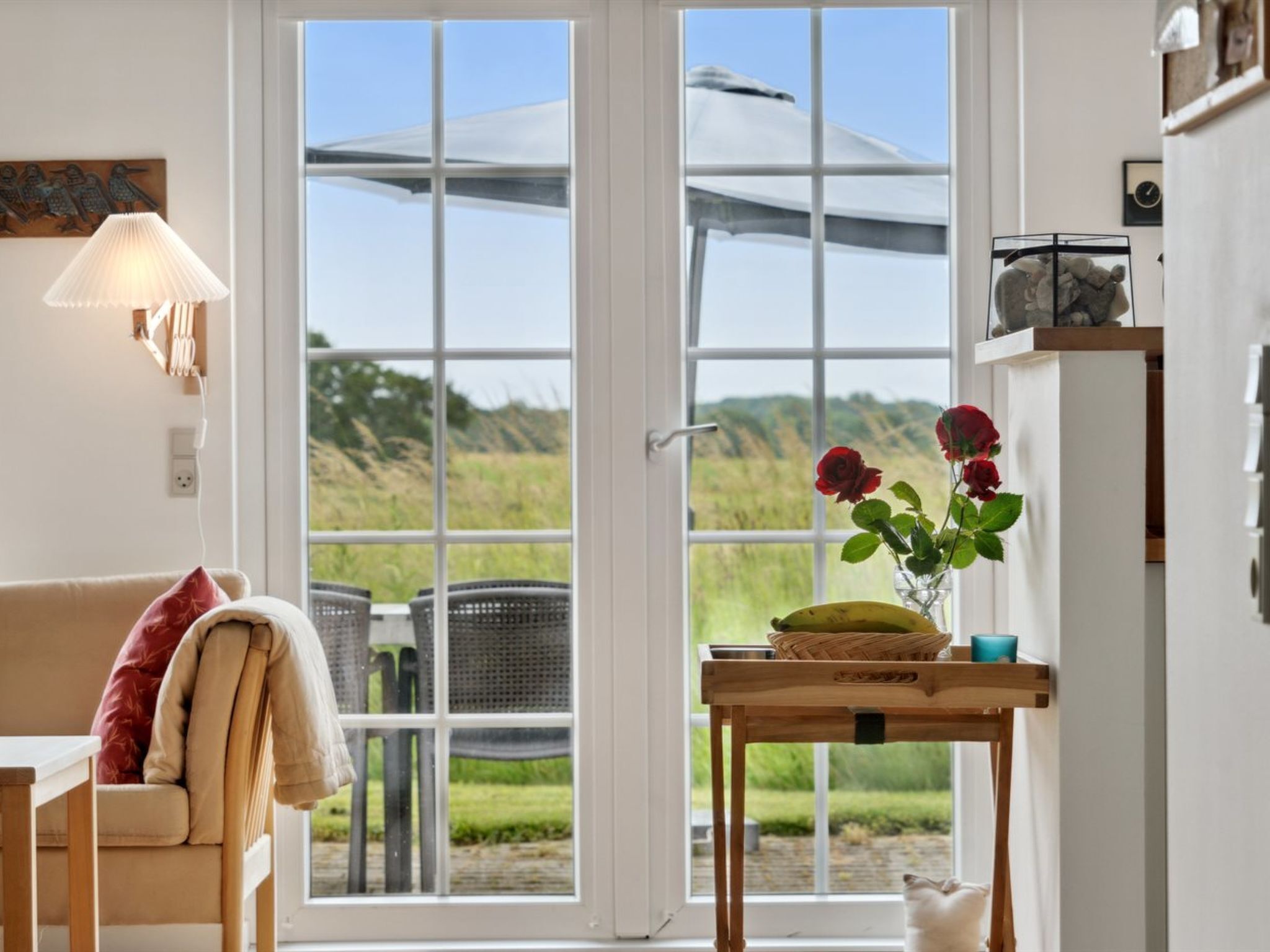 A cozy room with a sofa, a table with a vase of flowers, and a view of a garden through a large window.