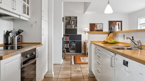 A modern kitchen with white cabinetry, a wooden countertop, and a built-in oven. There is a bookshelf in the background and a dining area with a table and chairs. - "Sakari" - 375m from the sea by Interhome (Brenderup Fyn)