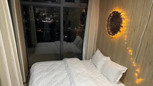 Een slaapkamer met een bed, nachtkastje, wandlamp en uitzicht op de stad door een glazen deur.