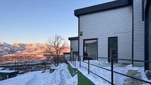 Een modern gebouw met een metalen hek en een groene wand, omringd door met sneeuw bedekte grond en bergen op de achtergrond.