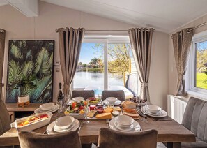 Un comedor con una mesa dispuesta para una comida, vista a un lago y un cuadro con temática tropical en la pared.