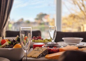 Une table à manger, dressée devant une fenêtre donnant sur des arbres et des immeubles, est garnie d’une variété de plats et de verres.