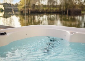 Un bain à remous rempli d’eau, entouré d’une étendue d’eau calme et avec des bâtiments en arrière-plan.