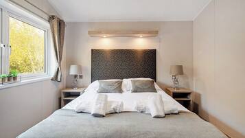 Une chambre d’hôtel moderne avec un grand lit, des tables de chevet, une fenêtre avec des rideaux et une tête de lit à motifs.