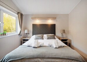 Une chambre d’hôtel moderne avec un grand lit, des tables de chevet, une fenêtre avec des rideaux et une tête de lit à motifs.